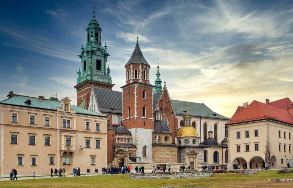 Traditional aged buildings and ancient Wawel Cathedral with various towers located on hill in Krakow against cloudy blue sky at sunset